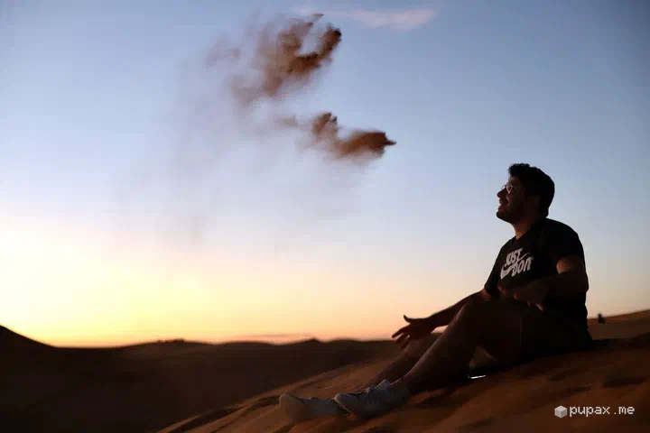 Una silhouette su una duna di Merzouga che lancia la sabbia al tramonto