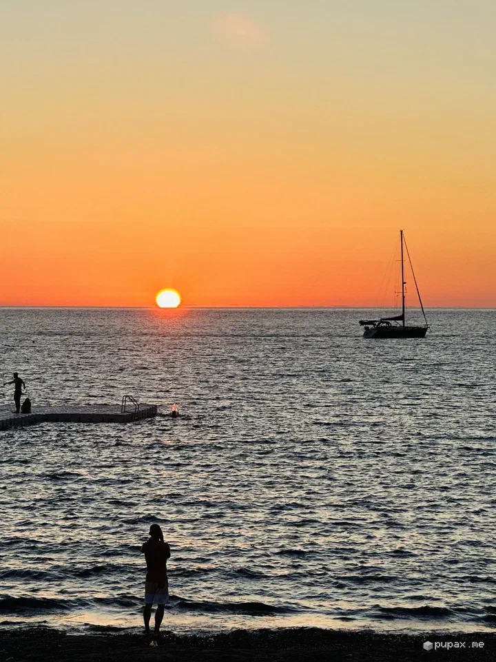 Il tramonto su Baia Cornino, con una barca a vela all'orizzonte