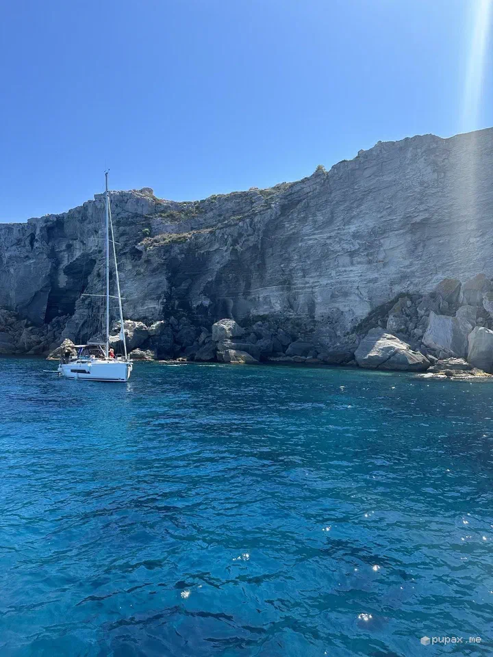 Una barca a vela ancorata sotto le pareti di tufo di Cala Rossa, a Favignana